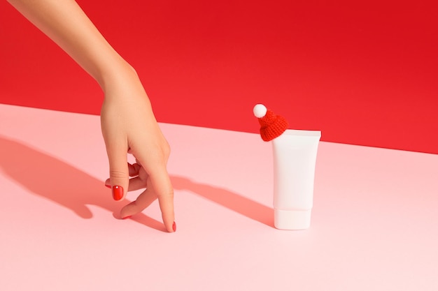 Womans hand with white plastic cosmetic tube on pink red background cosmetics sale concept