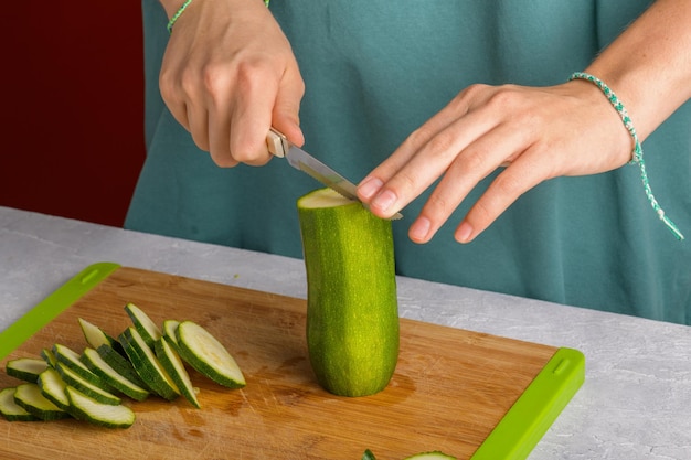 Womans hands cutting zucchini on wooden cutting board at home preparing healthy food close up