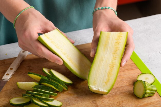 Le mani delle donne che tagliano le zucchine su una tavola da taglio in legno a casa preparano cibo sano da vicino