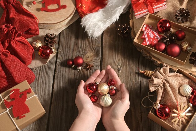 Womans hands hold Christmas balls on wooden table next to other gifts Authentic Christmas photo