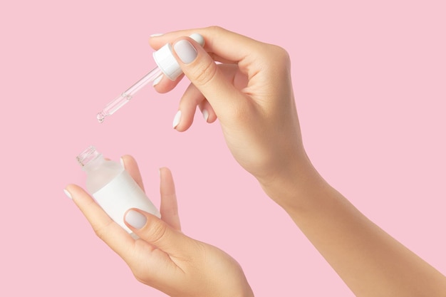 Womans hands holding dropper on pastel pink background self care beauty treatment concept