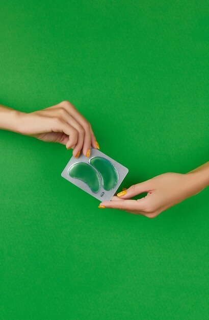 Womans hands holding eye patches on green backgound face care beauty treatment steps concept