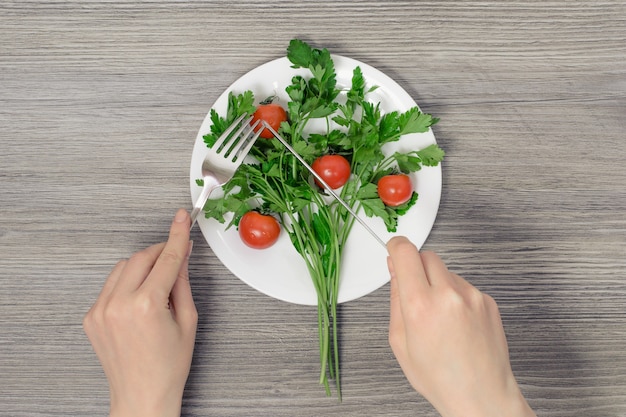 Womans hands holding fork and knife over plate with cherry tomatoes parsley