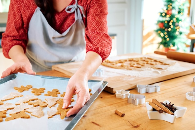 Photo womans hands putting cookies a shape of christmas gingerbread on oven paper