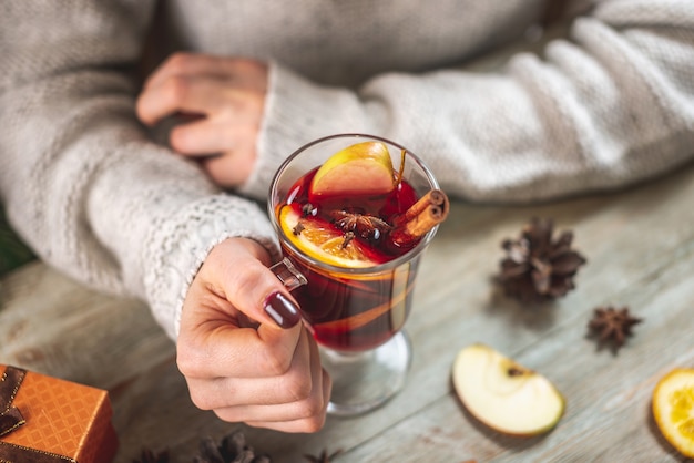 따뜻한 스웨터에 여자의 손은 나무 테이블에 향기로운 뜨거운 mulled 와인 한 잔을 들고있다