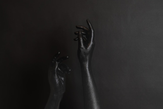 Womans hands with black paint on her skin on dark background High Fashion art concept