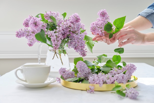 Le mani della donna con il mazzo di fiori lilla in brocca di vetro