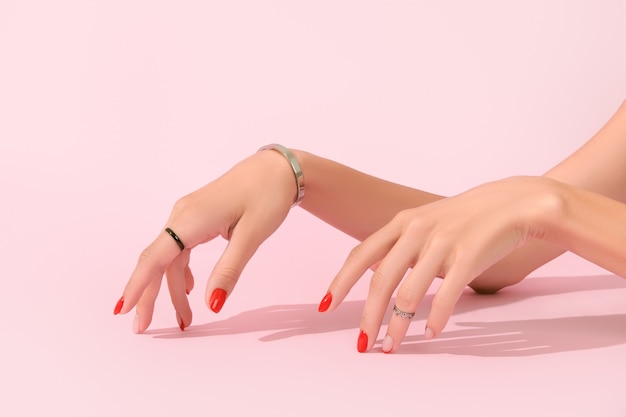 ピンクの背景のマニキュアデザイントレンドに赤いマニキュアと女性の手