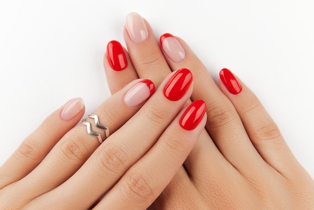 白い壁のマニキュアデザインのトレンドに赤いモダンなマニキュアと女性の手