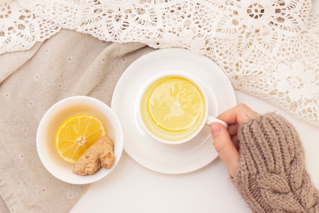 Womans hands with tea, lemon, ginger on white