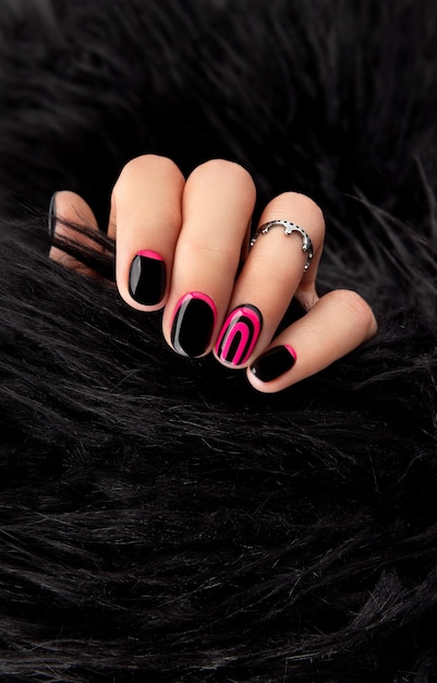 Womans hands with trendy pink and black manicure in fur coat.