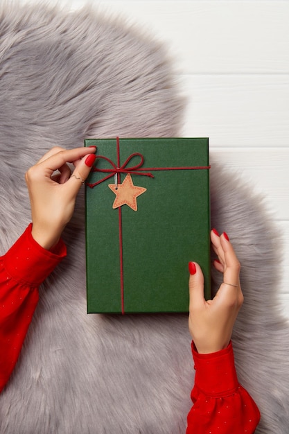 Womans hands with trendy red manicure holding gift box on fluffy carpet