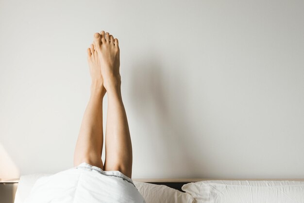 Photo womans legs in bed on the white wall resting or morning concept selective focus