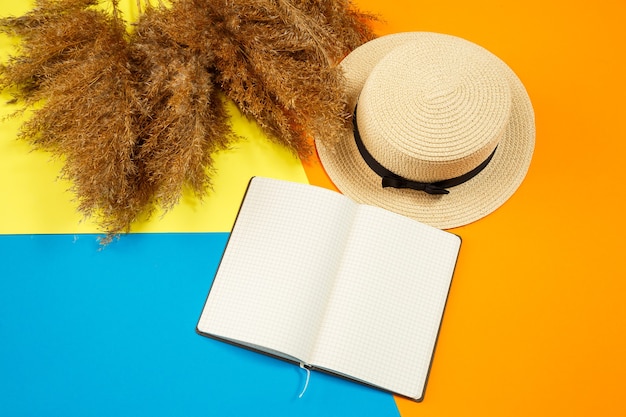 Women accessories notebook, hat, lifestyle, woman, relax, with dry grass, decor, flat lay, color style on the background. Travel, tourism concept. Beach accessories top view.