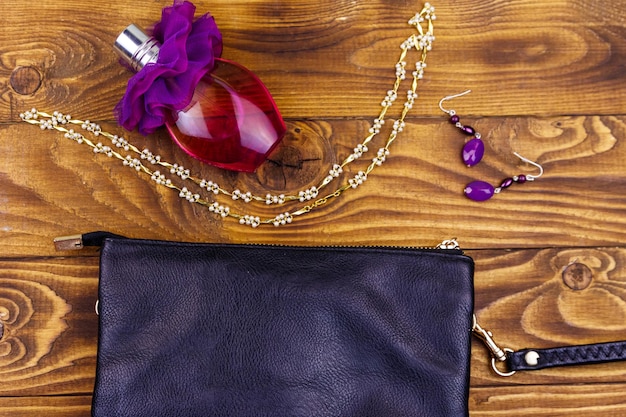 木製の背景に女性のアクセサリー香水の真珠のネックレスのクラッチバッグボトルと木製のテーブルのイヤリング美しさとファッションの構成上面図フラットレイ