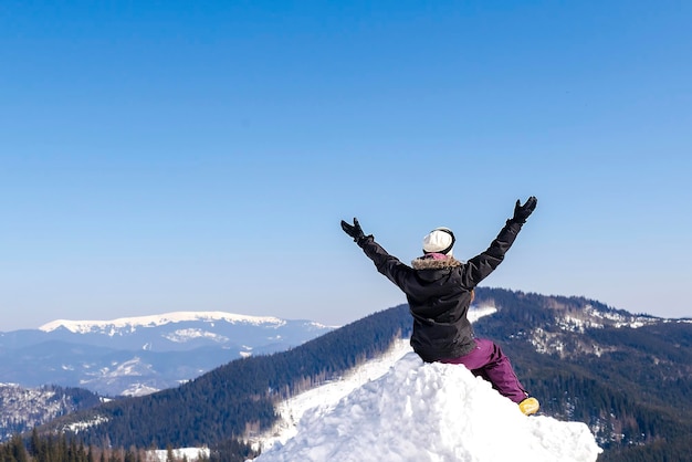 Women alpine girl in winter overalls sitting on snow hill looking at snow high Carpathian mountains at winter ski resort holiday outdoor nature landscape Ukraine Europeaerial view