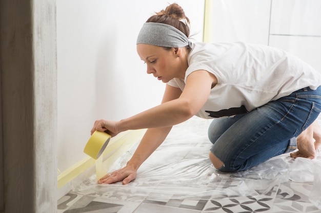 The women are preparing the wall for painting sticking masking\
tape to the wall