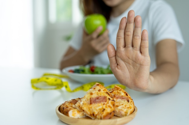 Photo women are rejecting and pushing pizza and eating apple, vegetable salads placed in front of them. women are choosing foods that are healthy for the body.