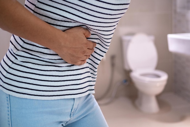 Photo women are standing in front of the bathroom door using their hands to hold the abdomen with severe abdominal pain or diarrhea the concept of stomach cramps diarrhea