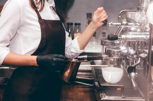 カフェでコーヒーを作るためにコーヒーマシンを使用している女性バリスタ