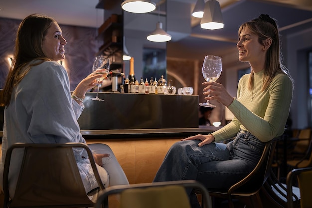 Foto le migliori amiche delle donne che bevono vino al bancone del ristorante - fidanzate che si divertono durante il fine settimana con in mano bicchieri di vino.