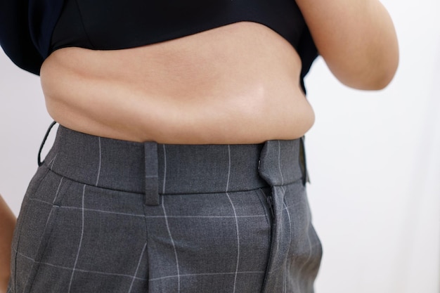 女性の体脂肪腹肥満の女性の手が過度の腹脂肪ダイエット ライフ スタイル コンセプトを持って腹を減らし、健康な胃の筋肉を形作る