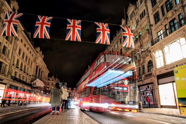 Women by blurred motion of bus with british flags hanging in city at night