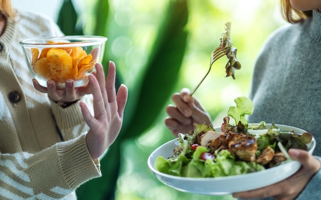 Photo women choosing to eat potato chips and making hand sign to refuse a vegetables salad                             person