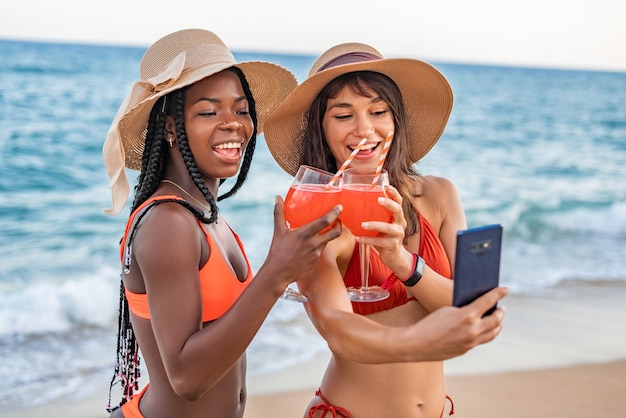 Women clinking drinks and taking selfie on beach