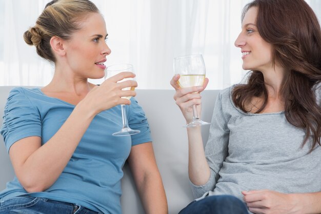 Photo women clinking their wine glasses while sitting on the sofa