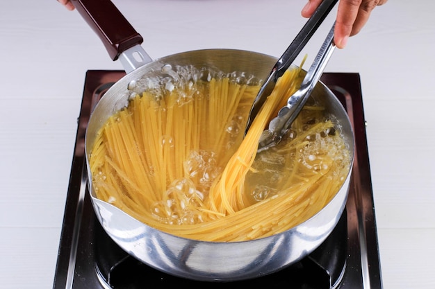 Women Cooking Spaghetti in Pan of Boiling Water in the Kitchen