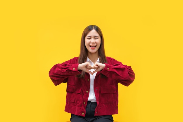 Donne che fanno gesto a forma di cuore con entrambe le mani e felicità sorridente su sfondo giallo isolato