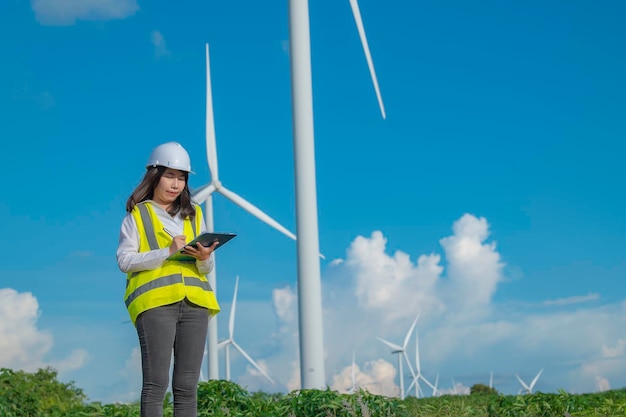 Women engineer working and holding the report at wind turbine farm Power Generator Station on mountainThailand people