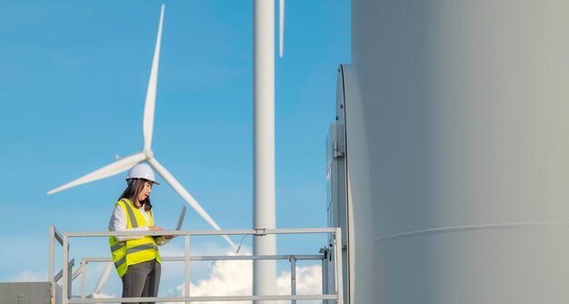 Women engineer working and holding the report at wind turbine farm Power Generator Station on mountainThailand people