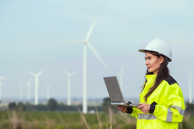 women engineer working and holding the report at wind turbine farm Power Generator Station on mountainThailand people