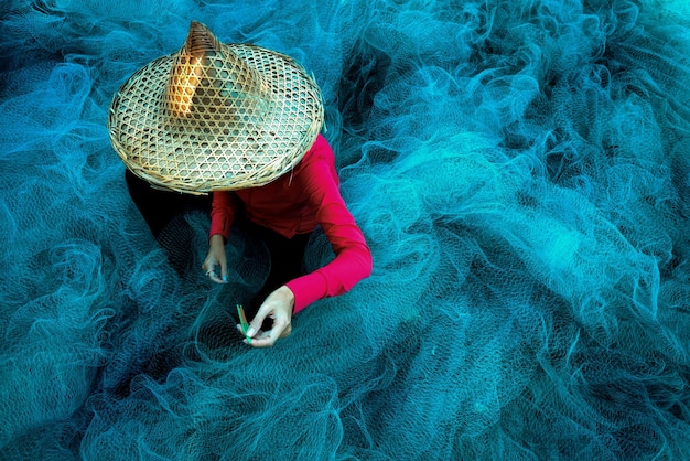 Women fisherman hands sewing blue fishing nets sitting on the ground and surrounded big net