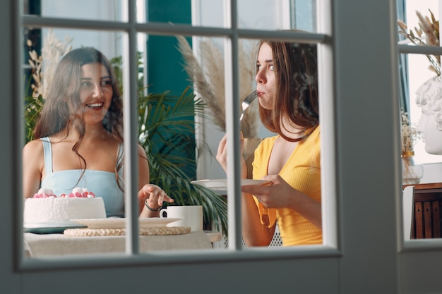Amici delle donne a casa seduti e sorridenti con una torta di compleanno bianca dietro la porta di vetro.