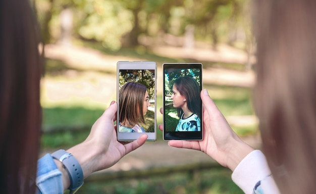 Women friends showing smartphones with their side view portraits photos taked over a forest background