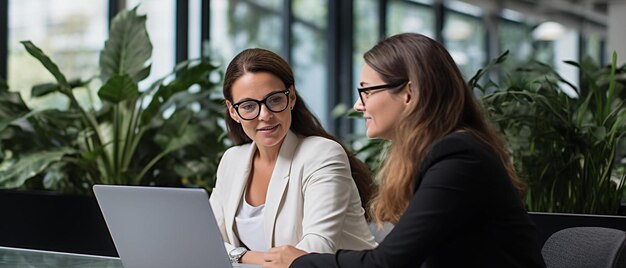 メガネをかぶった女性がラップトップに座りそのうちの1人は自分のコンピューターを見ています