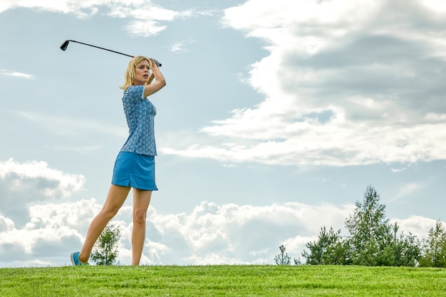 Время игры в гольф женщин держа оборудование гольфа на зеленом поле