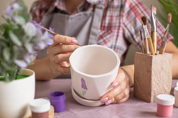 Photo women in gray apron paint a white flower ceramic pot