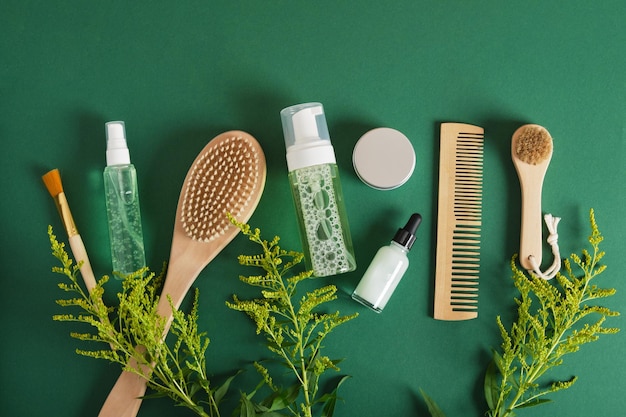 Women hair care set Comb wooden brush gel jar dropper bottle on green background top view