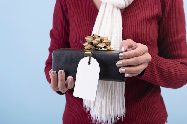 クリスマスと新年のコンセプトの白い背景に分離された黒いギフトボックスと紙タグを持つ女性の手。