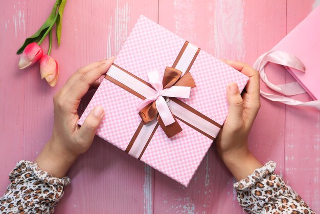 Women hand holding pink color gift box, top view .