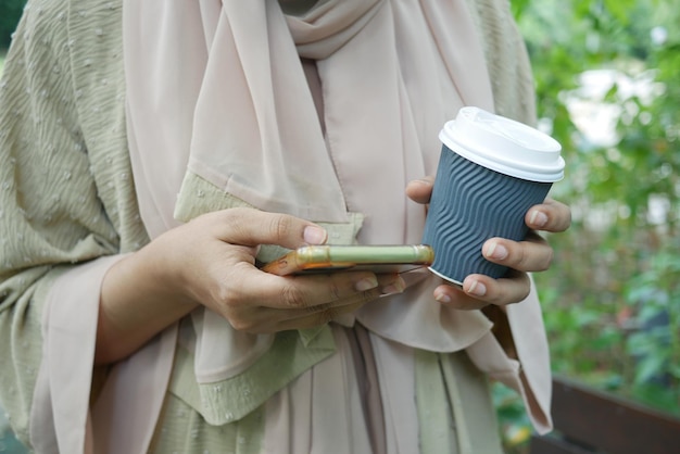 Mano delle donne che tiene smartphone e tazza di caffè di carta