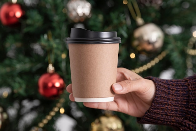 크리스마스 트리 배경으로 테이크 아웃 커피 컵을 들고 있는 여성