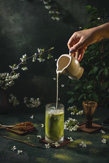 Women hand is pouring homemade sour cream from small jar to glass with matcha tea