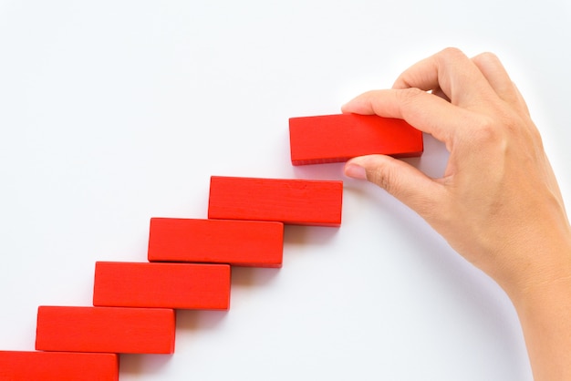 Women hand put red wooden block on yellow wooden blocks in the shape of a staircase