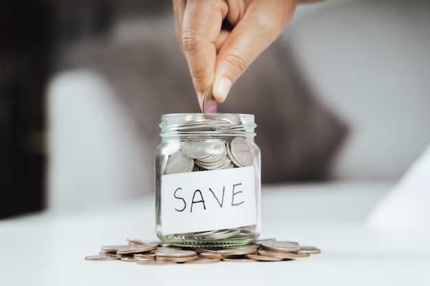 Women hand putting money coin into glass jar for saving money. saving money and financial concept