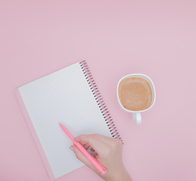 Mano delle donne con la scrittura sul taccuino in bianco su sfondo rosa, instagram e concetto di business.